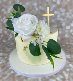 single tier christening cake with artificial flowers and golden cross