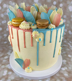 single tier naming day cake with blue and pink drip, topped with macarons
